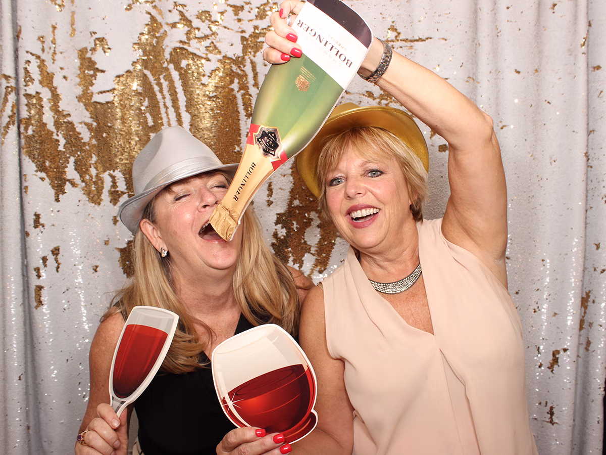 Deb Newman, founder of Photo Magic Events, posing with custom props in a photo booth rental with a friend